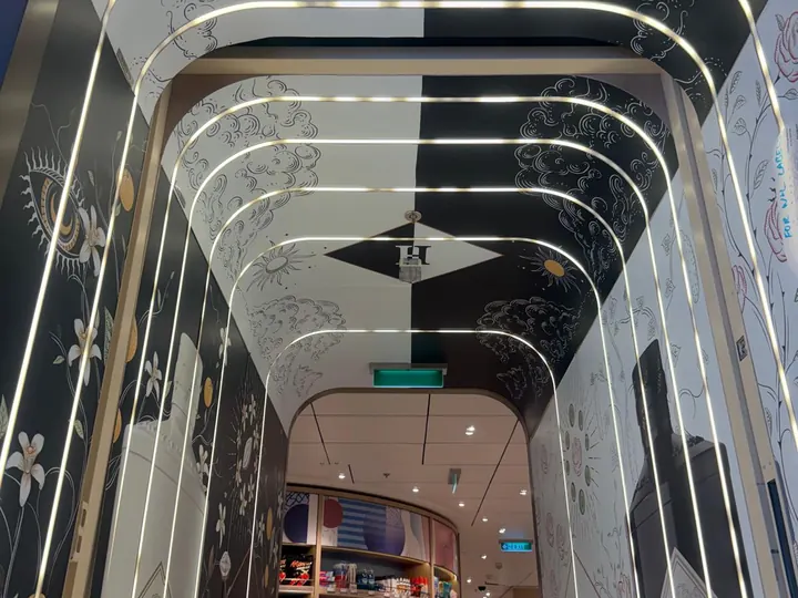Illuminated walkway with decorative wall graphics leading into a travel retail shop