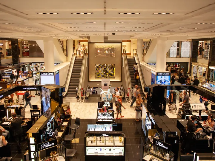Busy department store beauty hall with cosmetics counters and escalators
