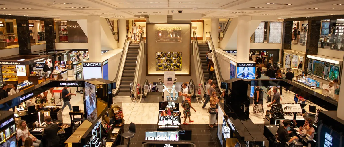 Busy department store beauty hall with cosmetics counters and escalators