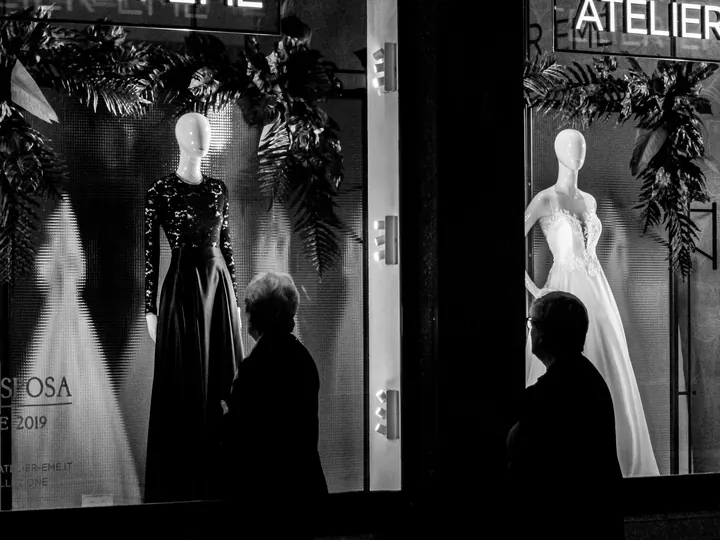 Shoppers passing illuminated retail window displays with mannequins