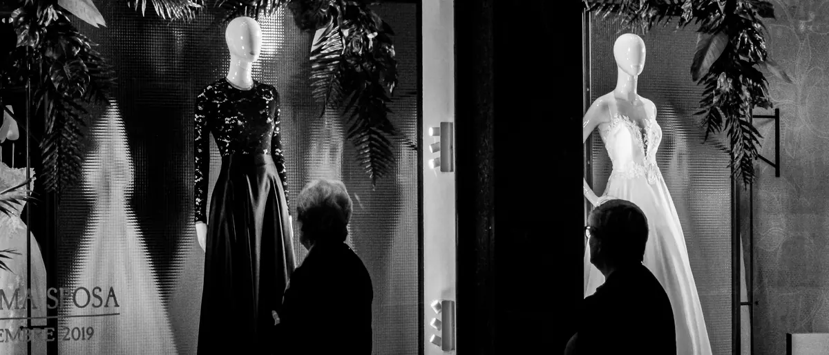 Shoppers passing illuminated retail window displays with mannequins